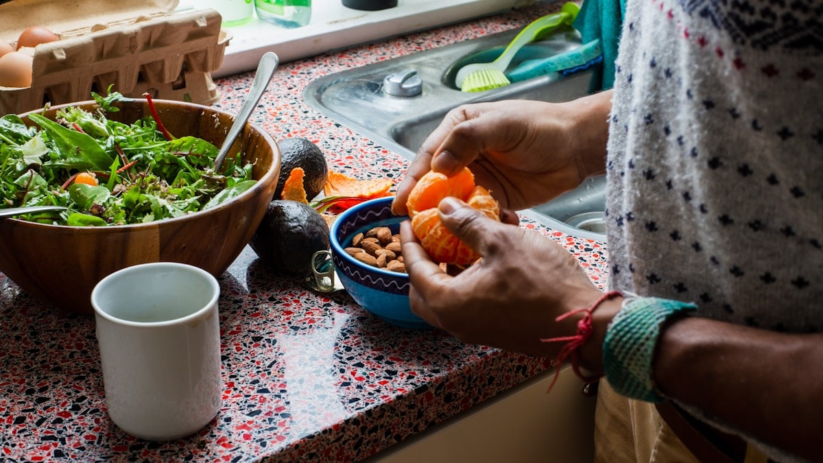 person holding orange fruit on blue ceramic bowl